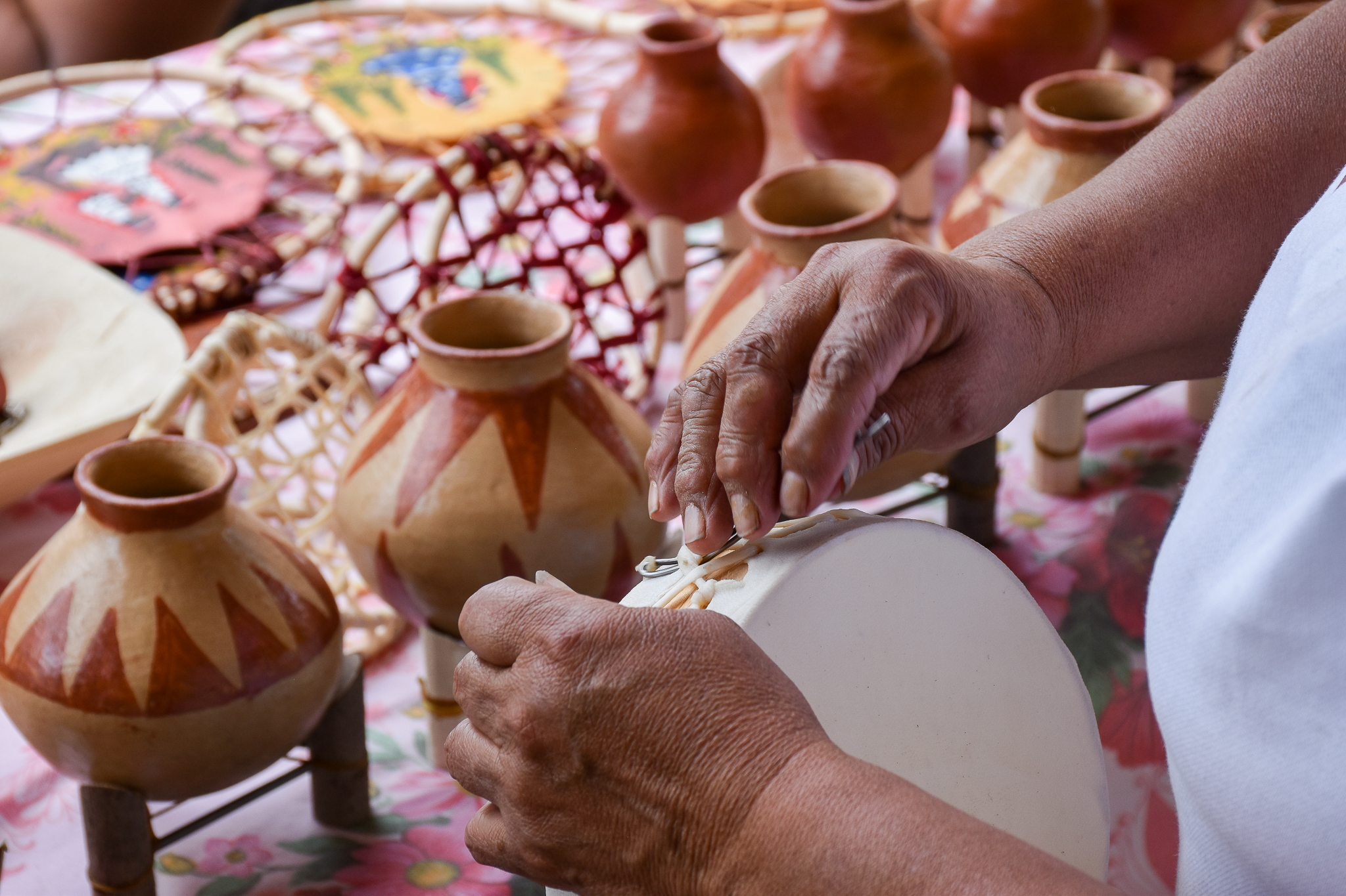 Manos de artesano tarahumara elaborando un instrumento tradicional con piel, rodeado de artesanías de barro